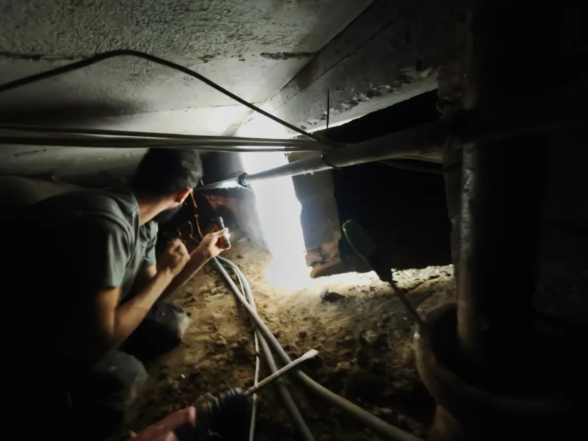 Technicien HelpDrain à la lampe frontale dans le vide sanitaire d'une maison à Uccle, curage des tuyaux un par un