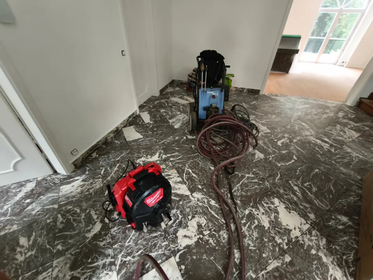 Machine de curage et hydrocureur installés dans le hall d'une maison à Uccle pendant le curage tuyau par tuyau